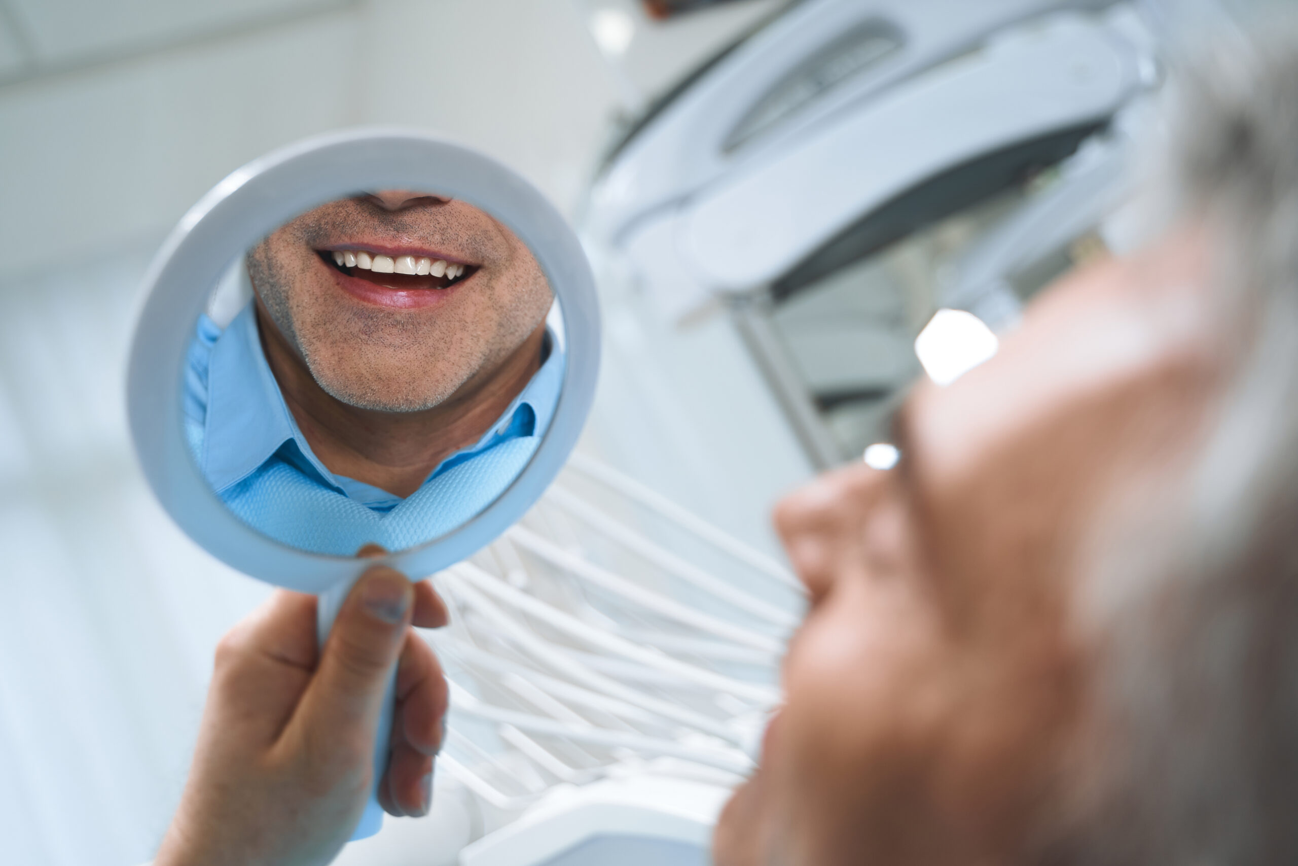 Man smiling in mirror after receiving dental implants.